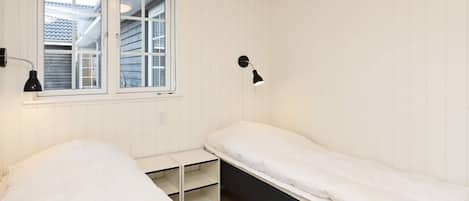 Una habitación con dos camas, un ventanal y una lámpara de pared.