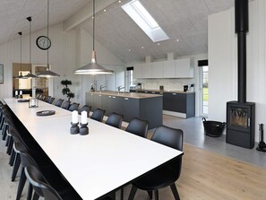 Une cuisine moderne avec une longue table à manger, des chaises noires, des luminaires suspendus et une cuisinière intégrée.