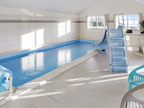 Una piscina interior con tobogán y escalera, y un ambiente soleado con ventana.