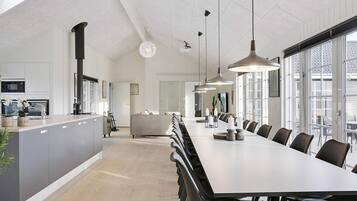 Una cocina moderna con una isla central, un comedor con una mesa larga y sillas, y ventanas amplias que dejan entrar luz natural.
