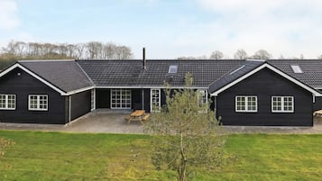A black building with a sloped roof, a covered patio area, and a small tree in the foreground.