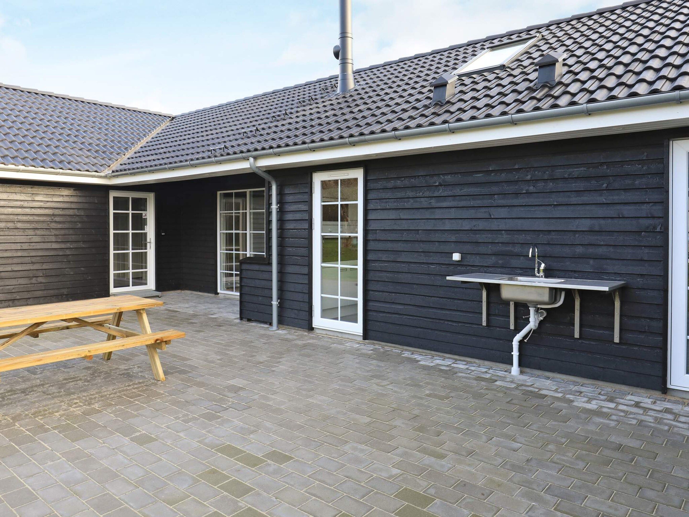 A building with a tiled roof, a black exterior wall, a sliding glass door, a wooden picnic table, and a built-in sink.