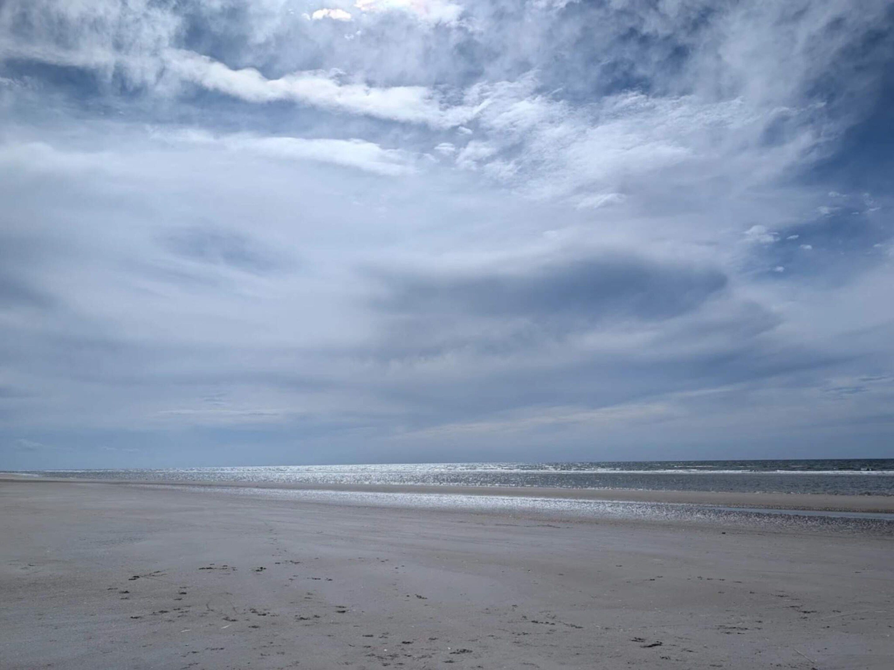 A beach with a wide sandy shore and a calm sea under a cloudy sky.
