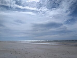 Une plage dotée d’un large rivage sablonneux et d’une mer calme sous un ciel nuageux.
