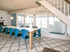A dining area with a large table and blue chairs, a staircase, and large windows. - 4 Star Holiday Home in Hirtshals (Hirtshals)