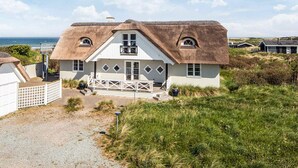 Uma casa costeira com telhado de palha, varanda e vista para o mar.