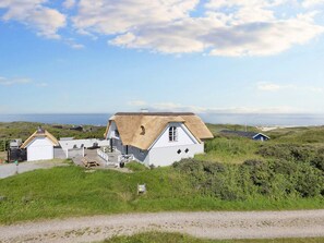 Un bâtiment blanc avec un toit de chaume, entouré de verdure et sous un ciel dégagé.