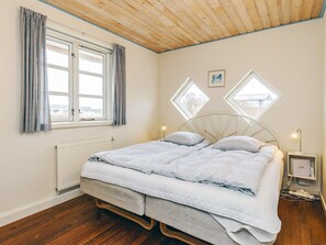 A bedroom with a bed, two windows, a radiator, and a nightstand with a lamp. - 4 Star Holiday Home in Hirtshals (Hirtshals)