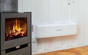 A wood-burning stove with a visible fire, a white wall, and a white electrical outlet.