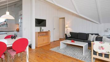 En rummelig loftrum med højt til loftet, et spiseområde med røde stole, en sofa og et TV ophængt på væggen.