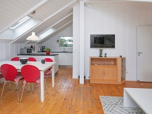 Una cocina moderna con zona de comedor, con una mesa blanca, sillas rojas, un mueble de madera y un amplio ventanal.
