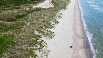 En vy över en strand sedd från luften, med sanddyner och en tydlig utsikt över havet.
