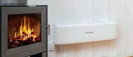 Un poêle à bois avec une flamme visible, un mur blanc et une prise électrique blanche.