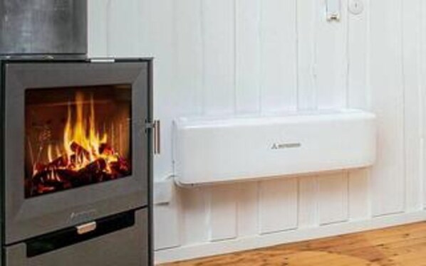 A wood-burning stove with a visible fire, a white wall, and a white electrical outlet.