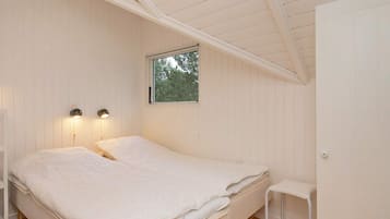 A bedroom with a single bed, two bedside lamps, a window, and a small white chair.