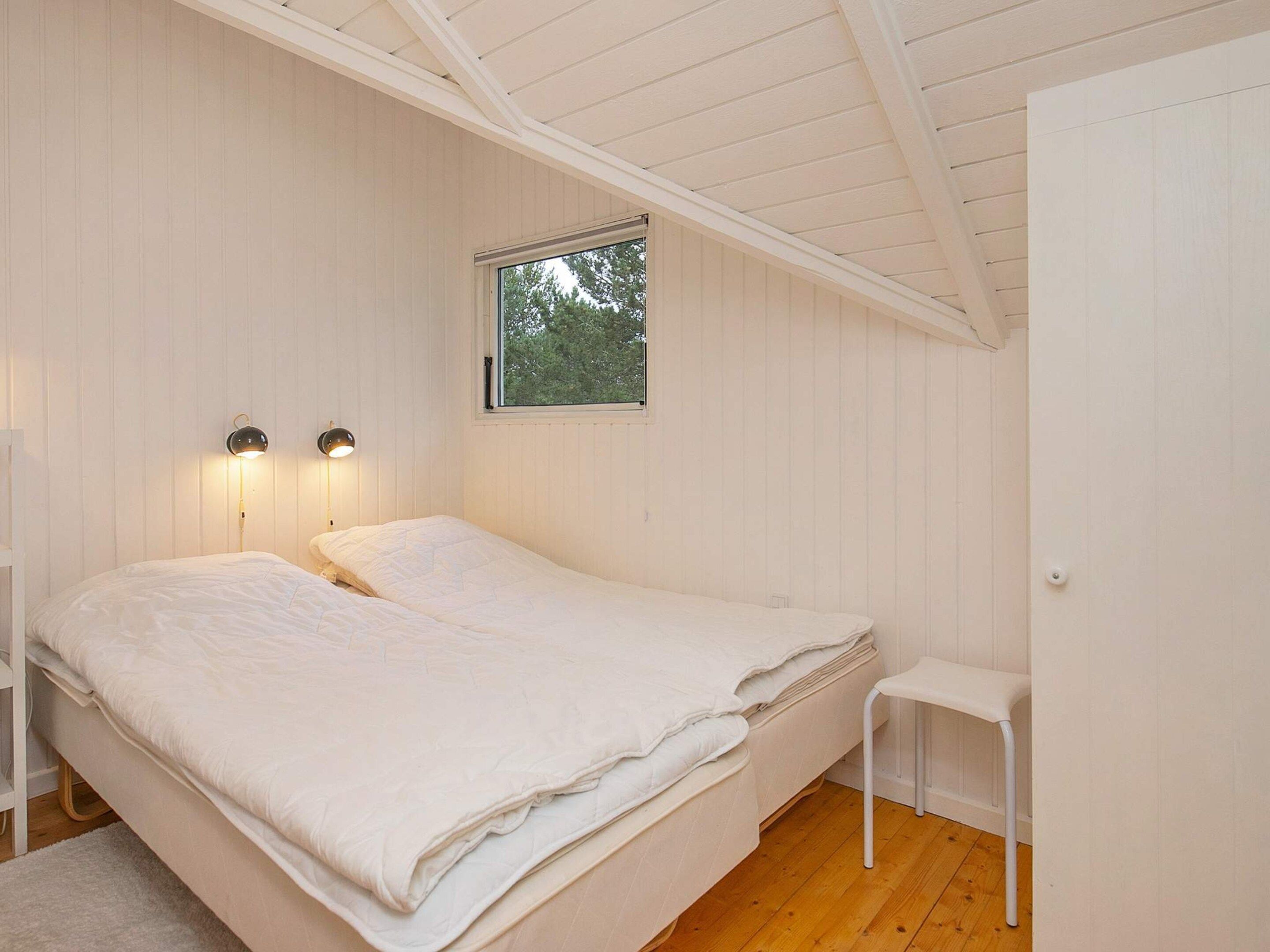 A bedroom with a single bed, two bedside lamps, a window, and a small white chair.