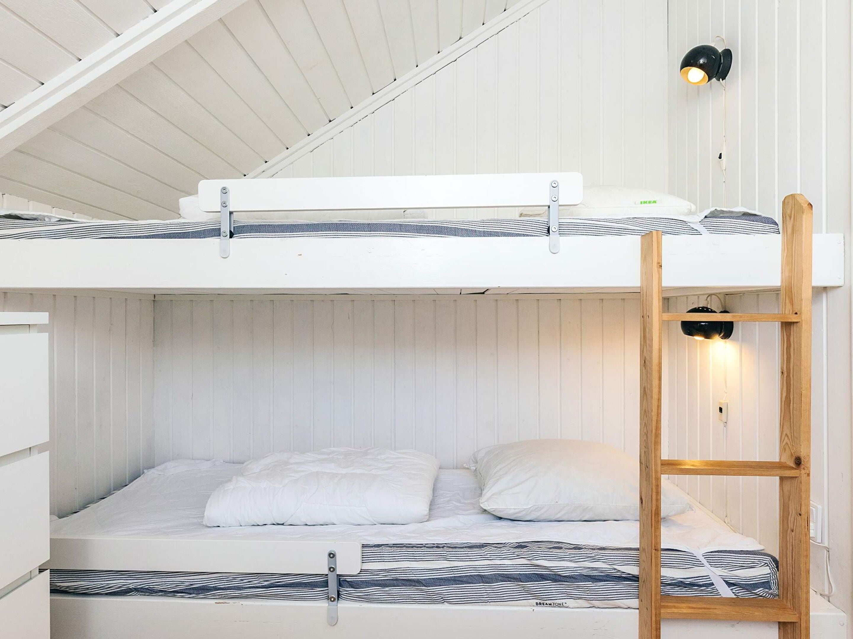 Ein Etagenbett mit einer Leiter, weißer Bettwäsche und einer Wandlampe.