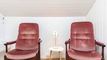 Deux fauteuils rouges à revêtement en tissu, avec des armatures en bois, une petite table blanche et un tapis à motifs sur un plancher en bois.