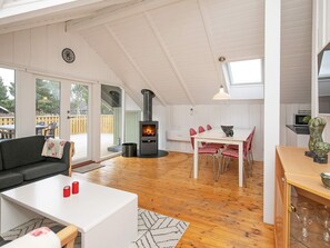 A cozy living room with a fireplace, a dining area with red chairs, and a kitchen with a microwave. - Lovely Holiday Home in Ã…lbÃ¦k near Sea (Aalbaek)