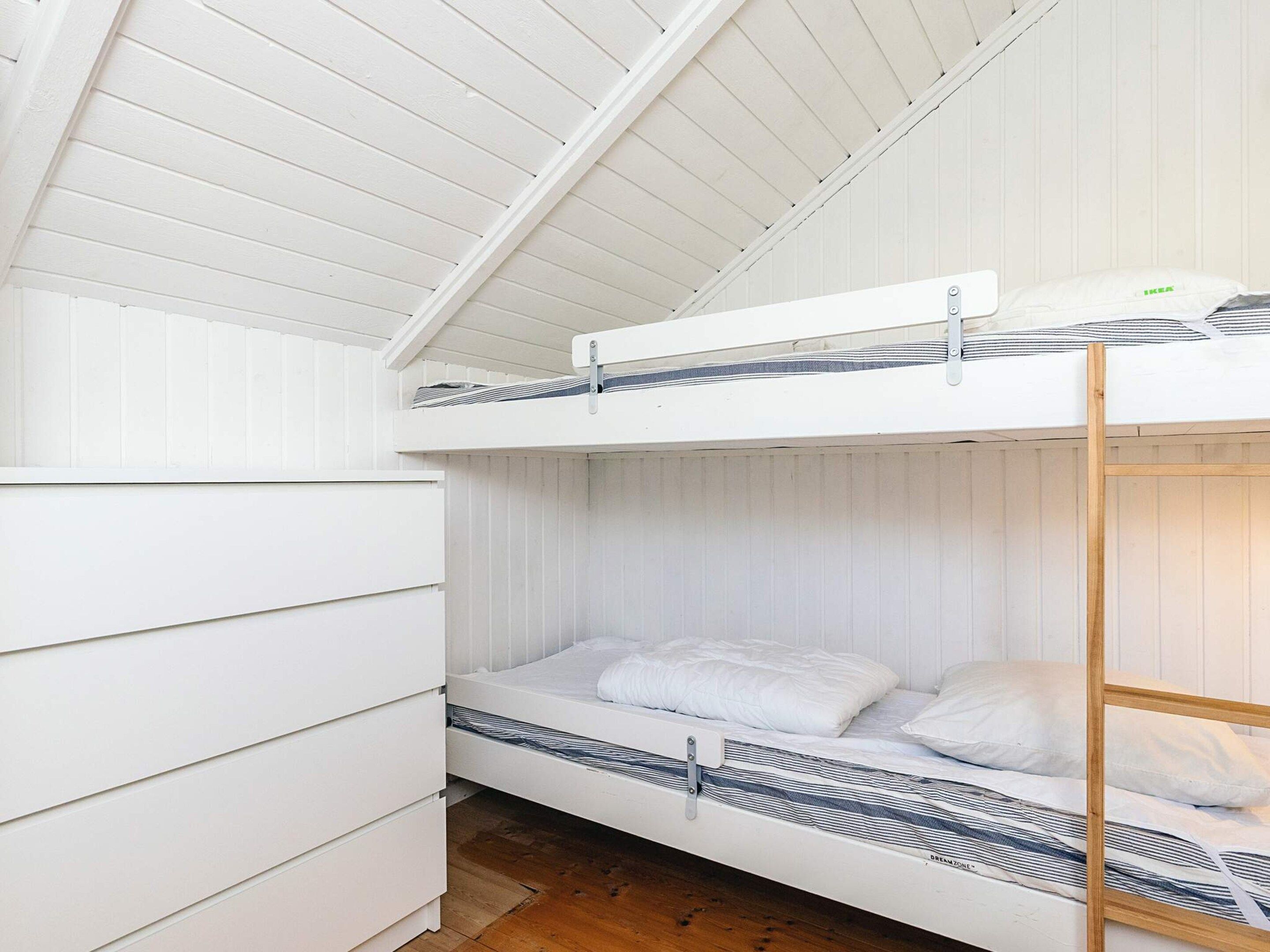 En køjeseng med en trætrap, hvide sengetøj og et hvælvet loft.