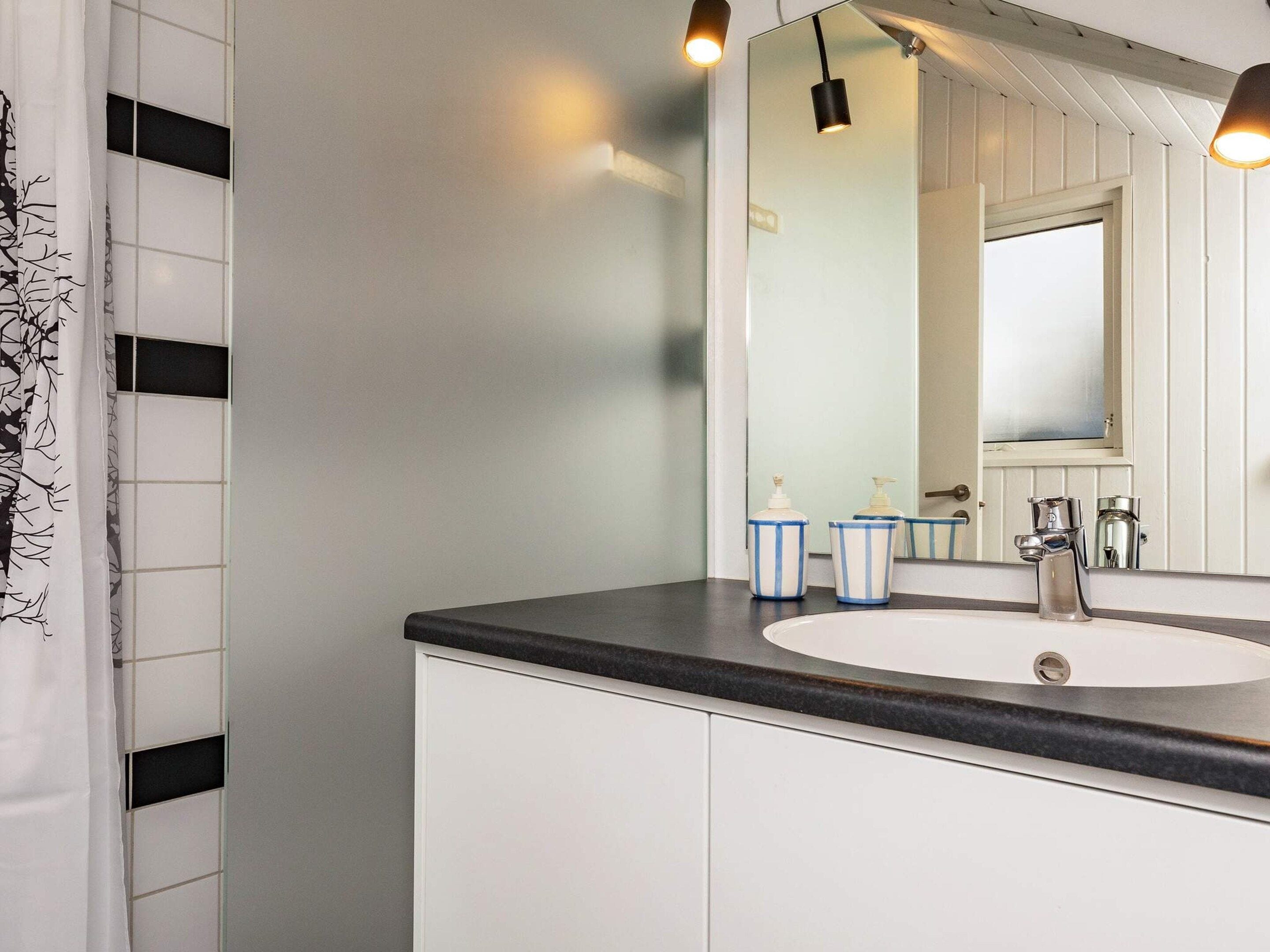 A bathroom with a white sink, a mirror, and two striped soap dispensers.