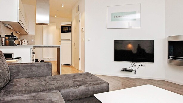 A modern living room with a grey sofa, a white coffee table, and a flat-screen TV mounted on the wall. - Holiday Home in Wendtorf (Wendtorf)