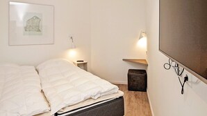 A bedroom with a bed, a bedside table, a lamp, a wall-mounted TV, and a framed picture on the wall. - Holiday Home in Wendtorf (Wendtorf)