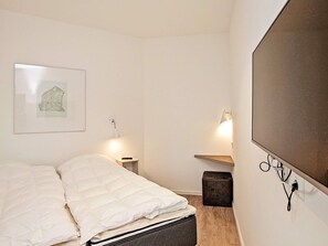 Quarto com cama, mesa de cabeceira, abajur, TV fixada na parede e um quadro enquadrado.
