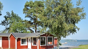 Eine rote Holzhütte mit Veranda, einer kleinen Terrasse und Blick auf das Wasser.
