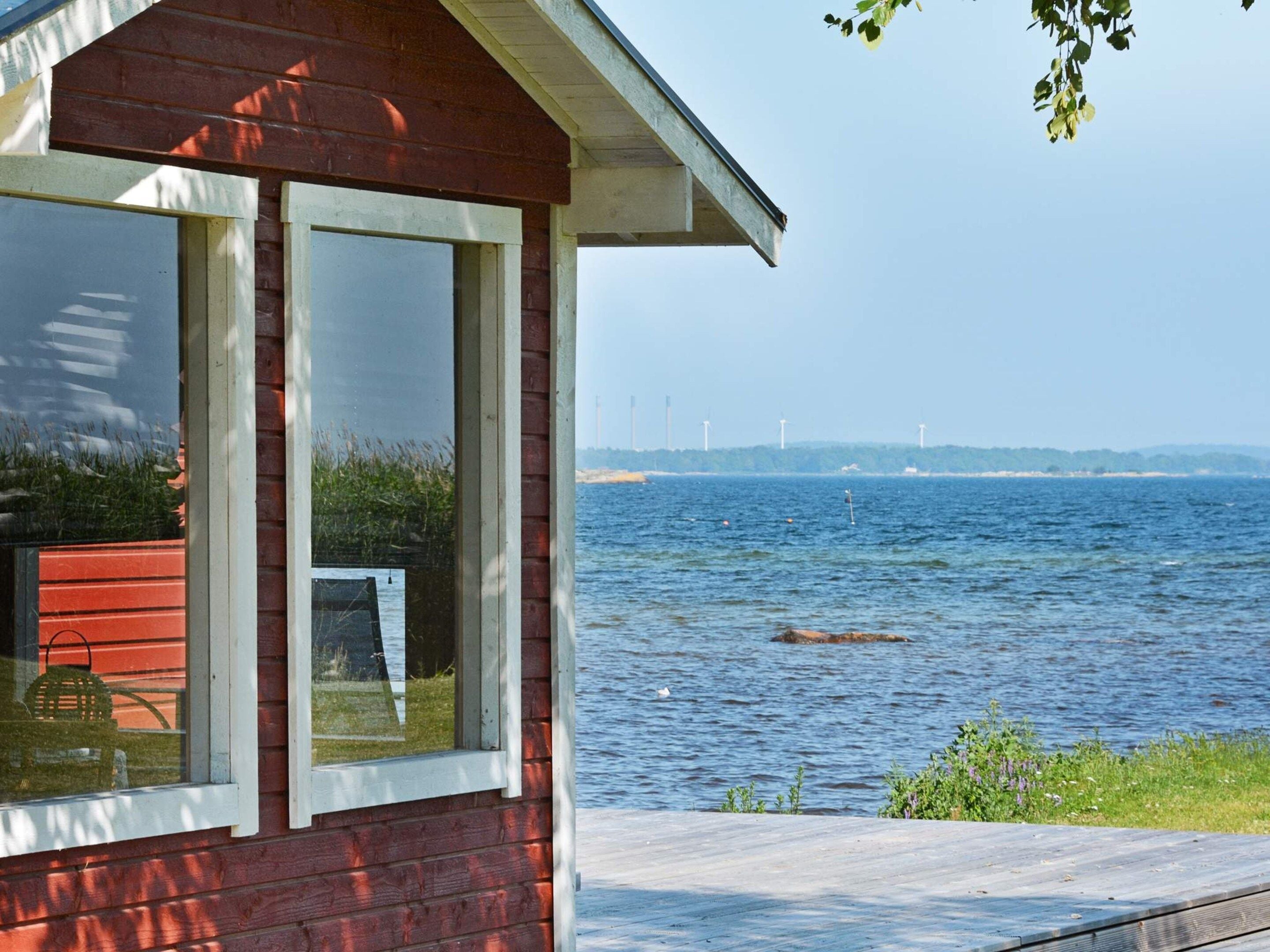 Eine rote Holzhütte mit einem großen Fenster mit Blick auf ein Gewässer.
