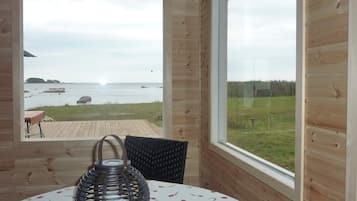 A wooden cabin room with a large window overlooking a beach and grassy area.