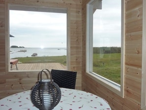 A wooden cabin room with a large window overlooking a beach and grassy area.