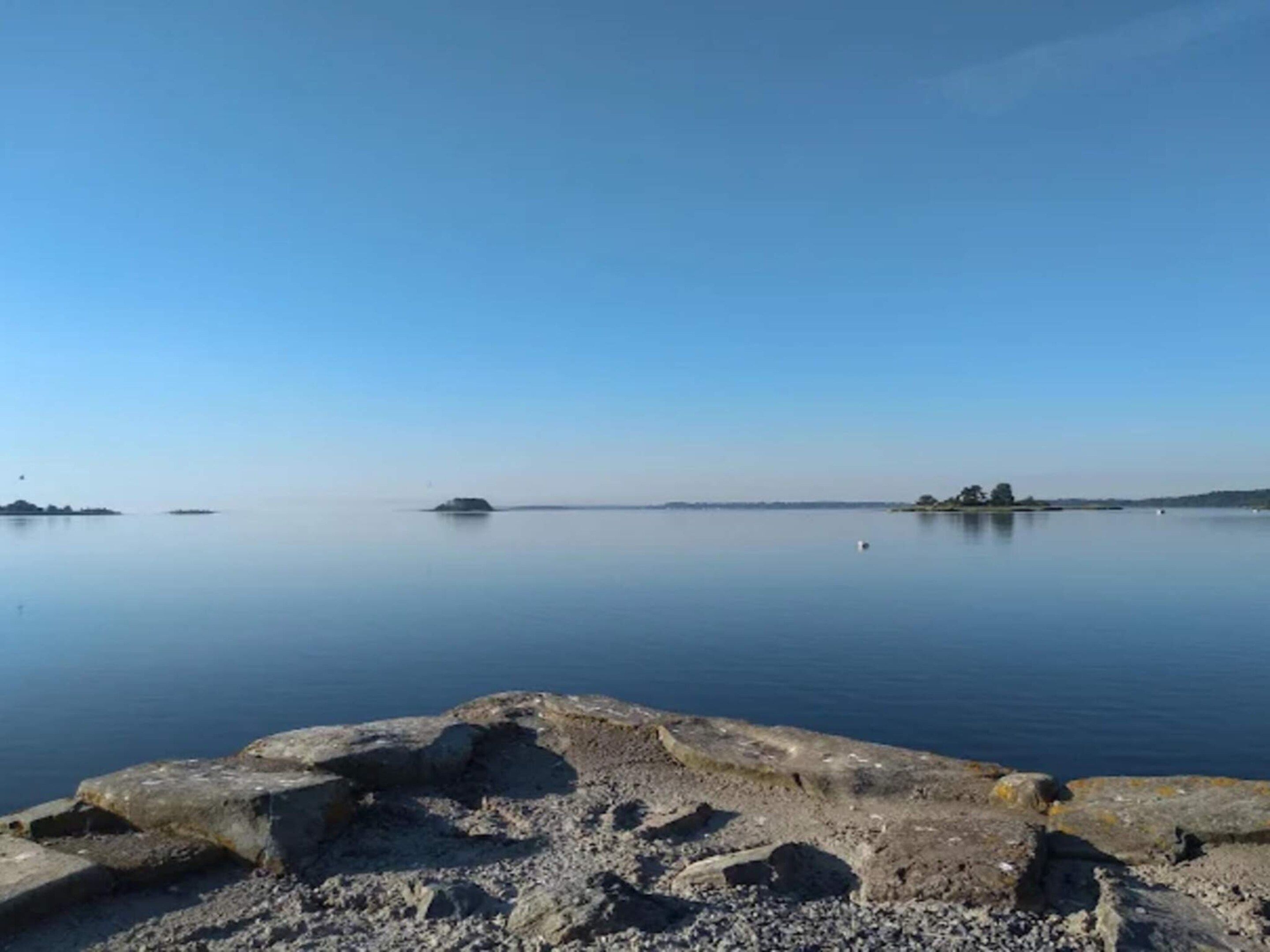 A calm lake with rocky shores and distant islands.