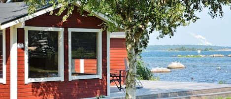 A red cabin with a dock extending into a lake, surrounded by greenery.