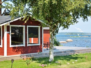 Una cabaña roja con un muelle que se adentra en un lago, rodeada de vegetación.