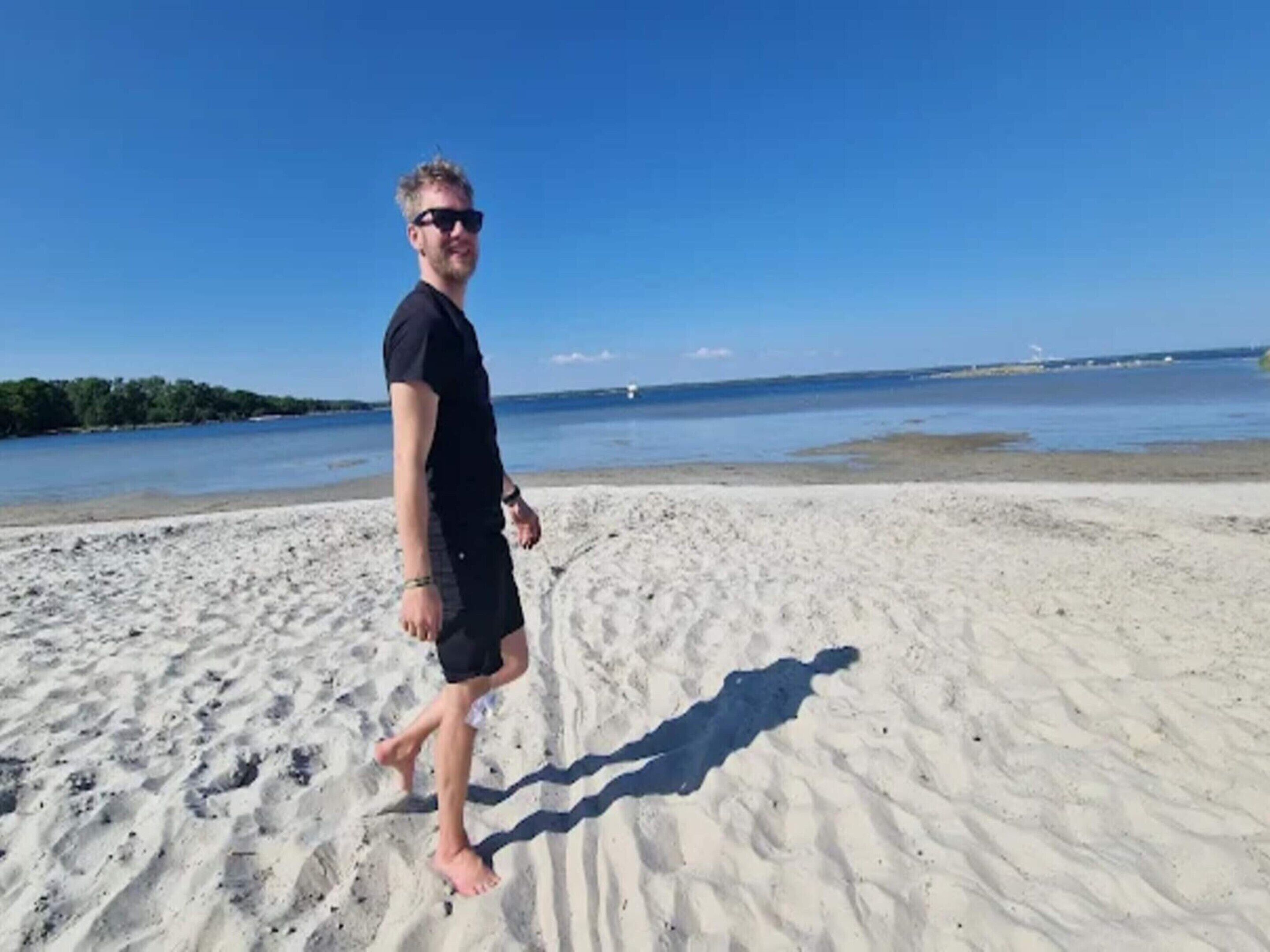A person walking on a sandy beach with a clear blue sky and calm water in the background.