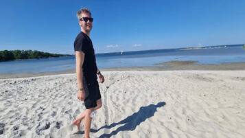 A person walking on a sandy beach with a clear blue sky and calm water in the background.