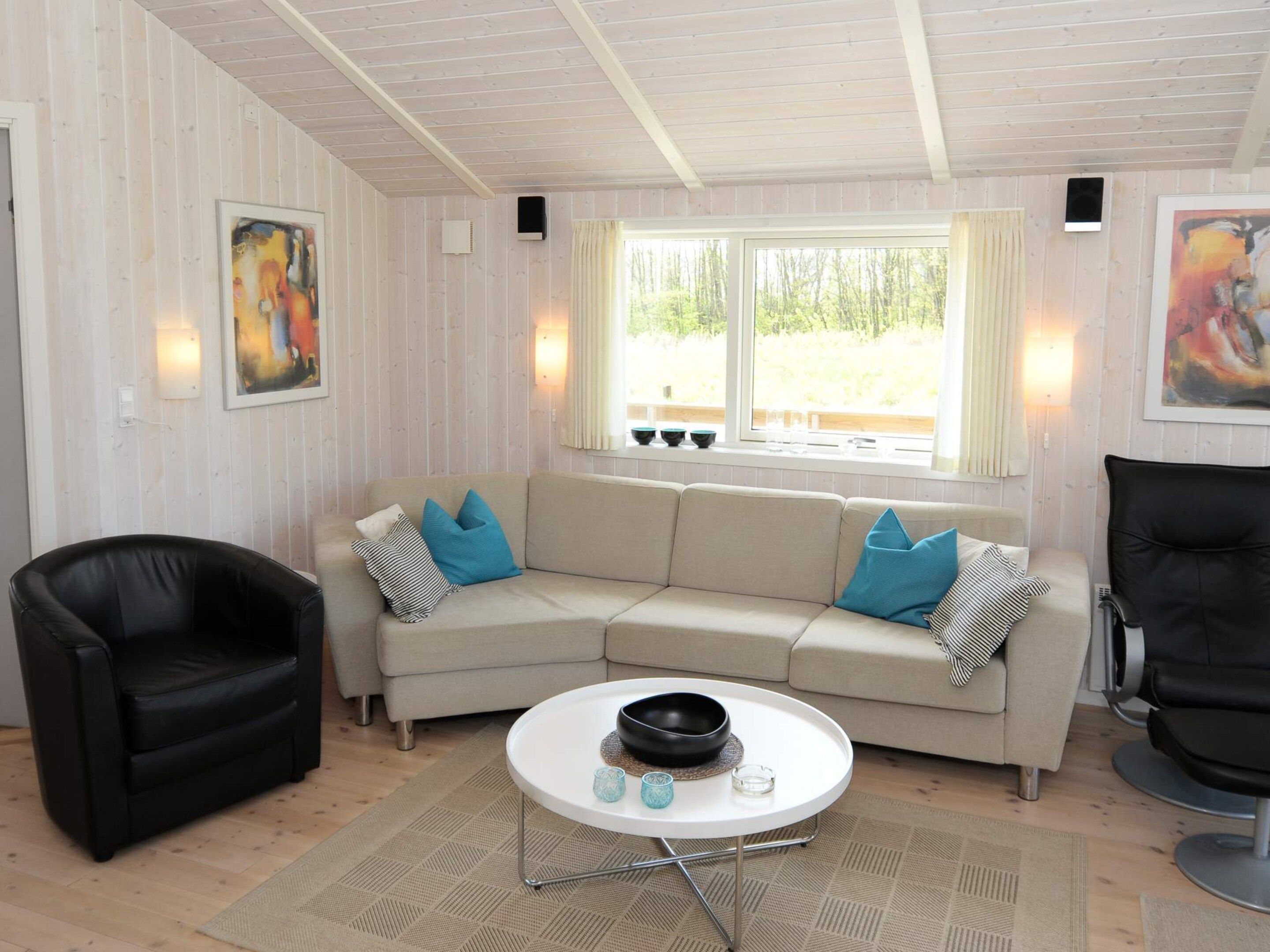Una sala de estar con un sofá color beige, un sillón de cuero negro y una mesa de centro blanca.