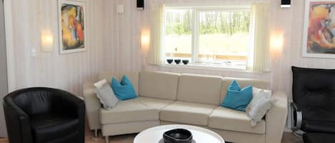 Una sala de estar con un sofá color beige, un sillón de cuero negro y una mesa de centro blanca.