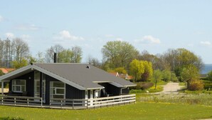 A modern house with a large deck, surrounded by a grassy field and trees.