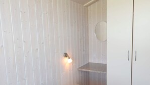 A bedroom with a bed, a nightstand, a wall-mounted light, a mirror, and a wardrobe.
