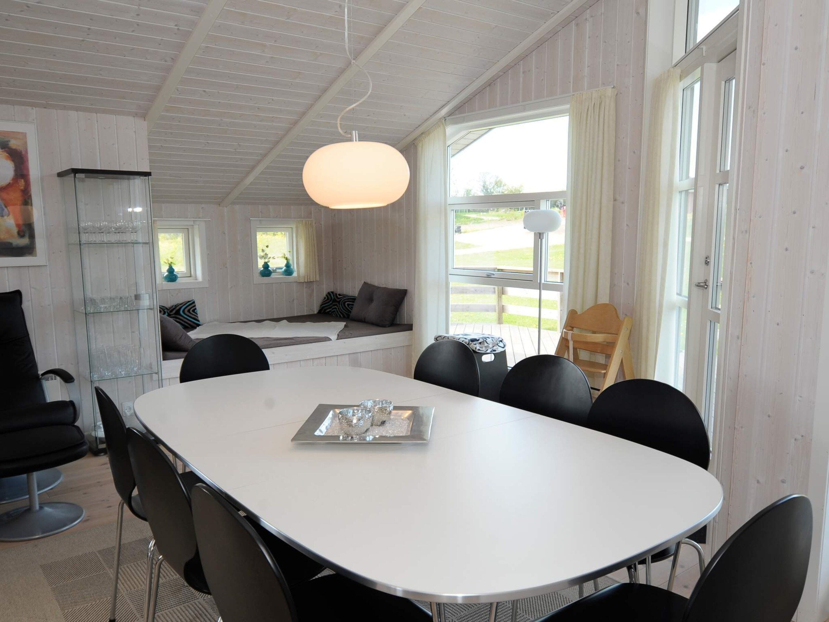 A dining area with a white table, black chairs, and a hanging light fixture.