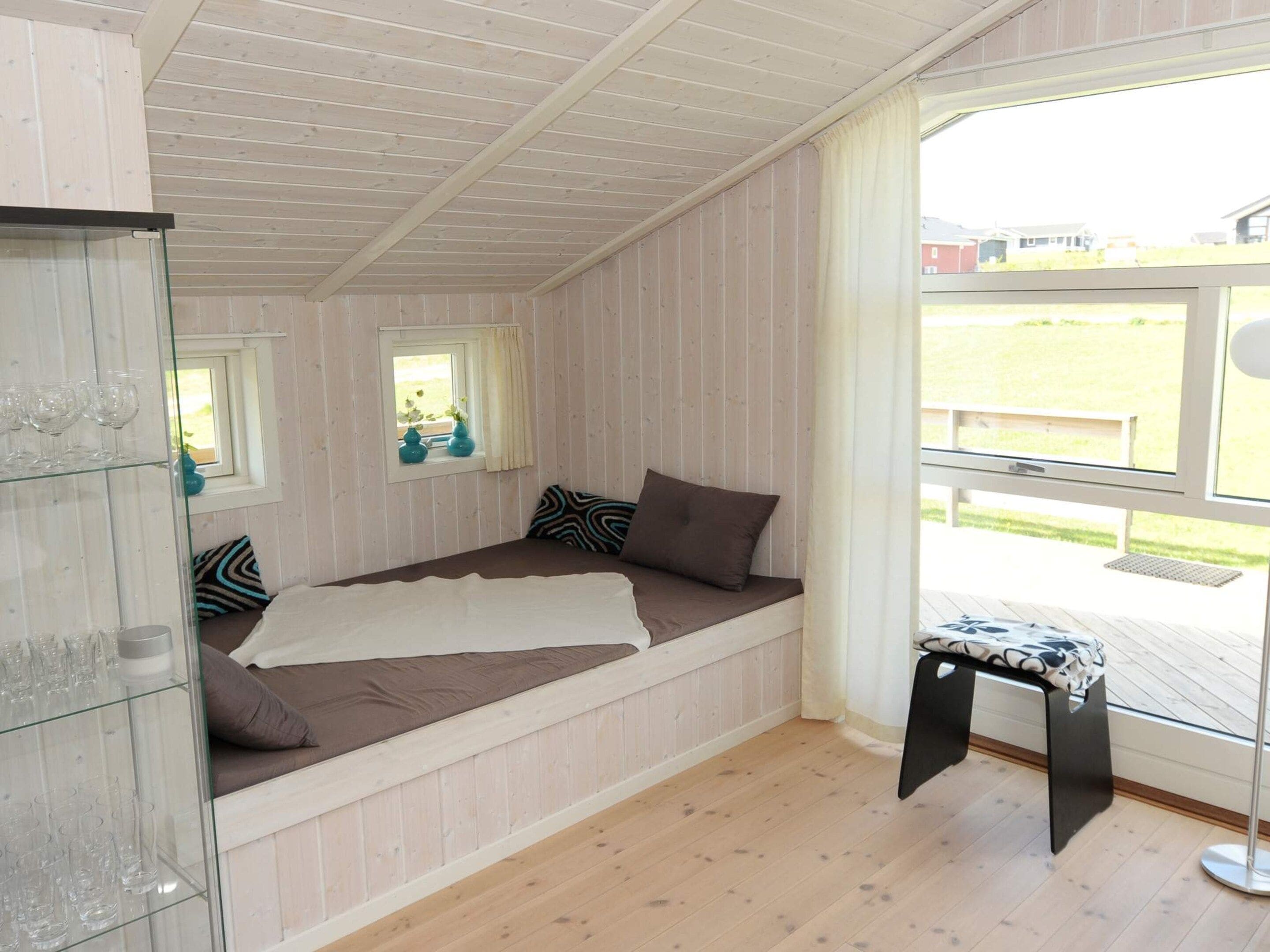 A room with a bed, a glass cabinet, a small table, and a window with a view of the outside.