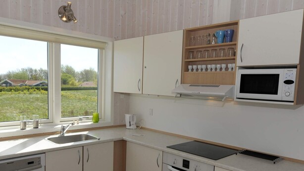 A modern kitchen with white cabinets, a built-in microwave, and a window with a view of the outdoors.