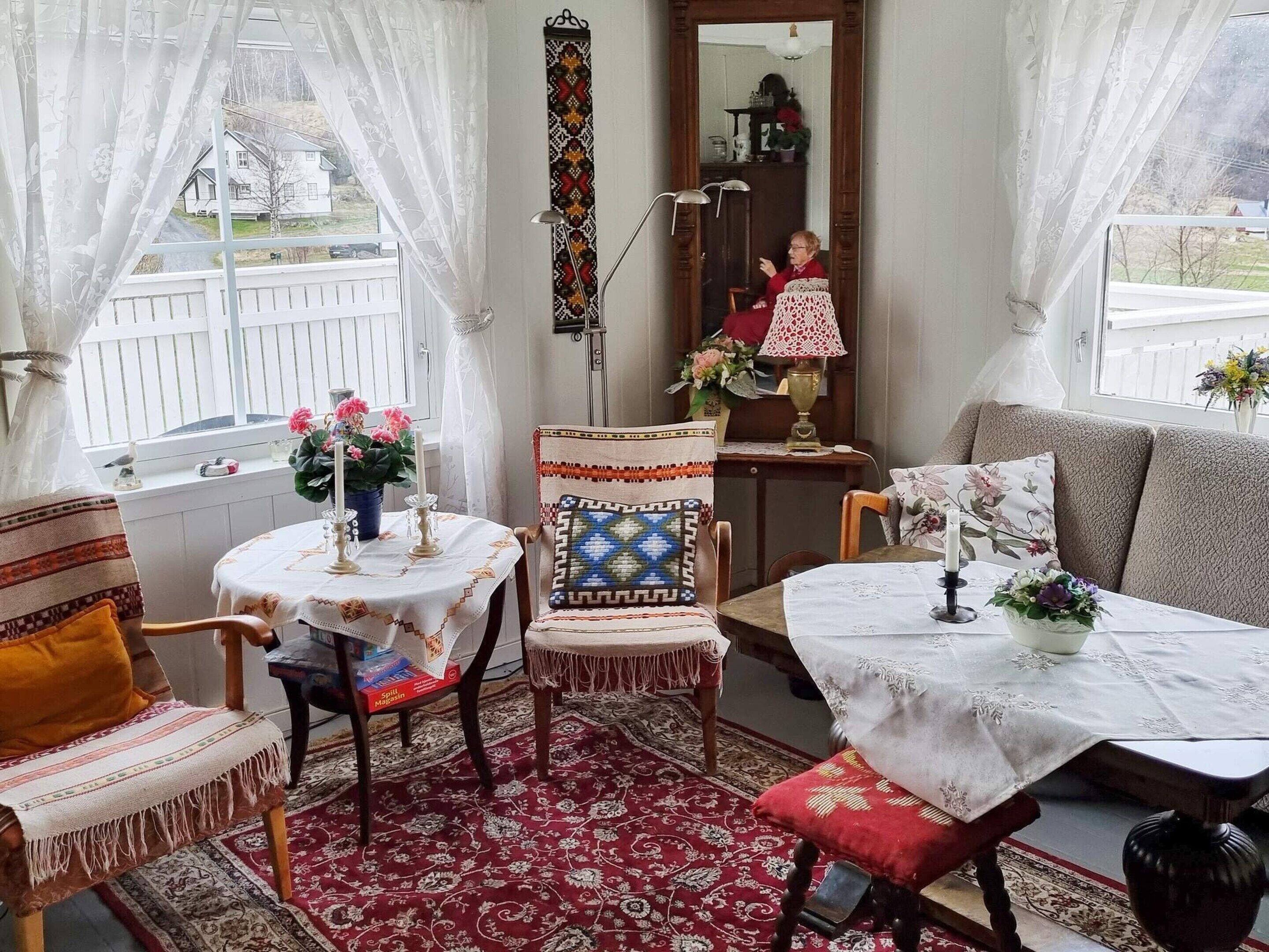A cozy room with a wooden chair, a sofa, a small table with a vase of flowers, and a mirror on the wall.