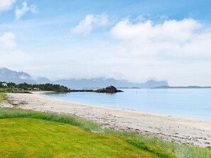 Et kystlandskab med en sandstrand, roligt vand og en lille rød bygning på en mole.