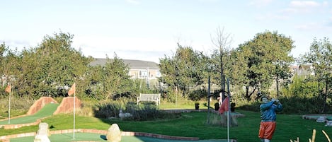 A miniature golf course with a putting green, sand traps, and a statue of a golfer.