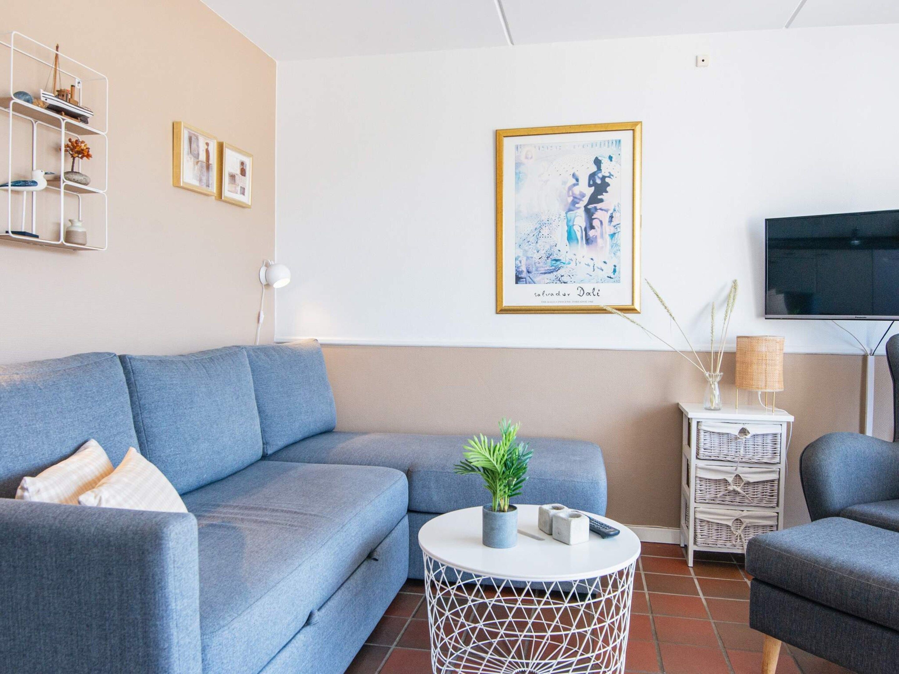 A living room with a blue sofa, a round coffee table, a TV, and a framed artwork on the wall.