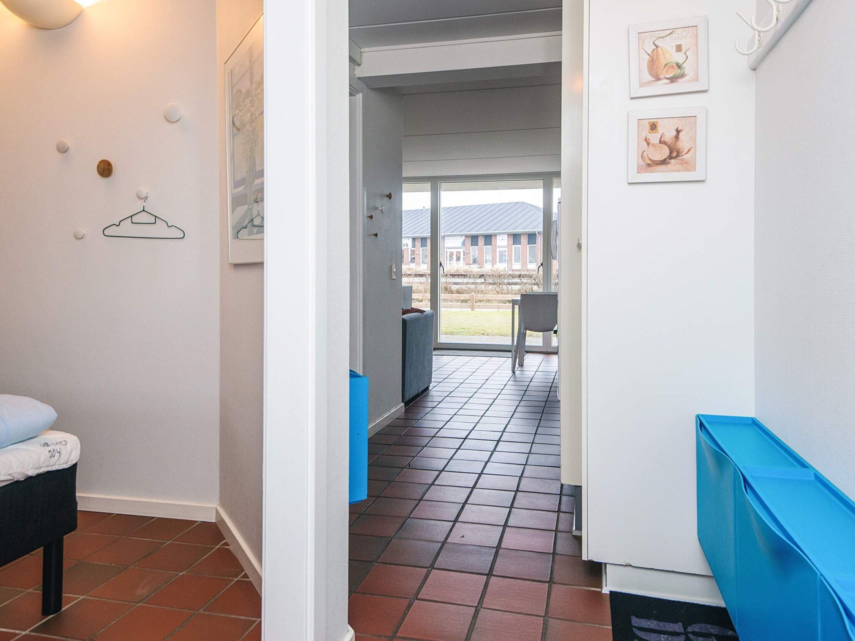 A hallway with a bed, a chair, and a blue bench. There are framed pictures on the wall and a window with a view of the outside.