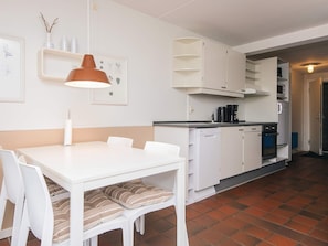 A modern kitchen with white cabinets, a dining table with chairs, and a hanging pendant light.